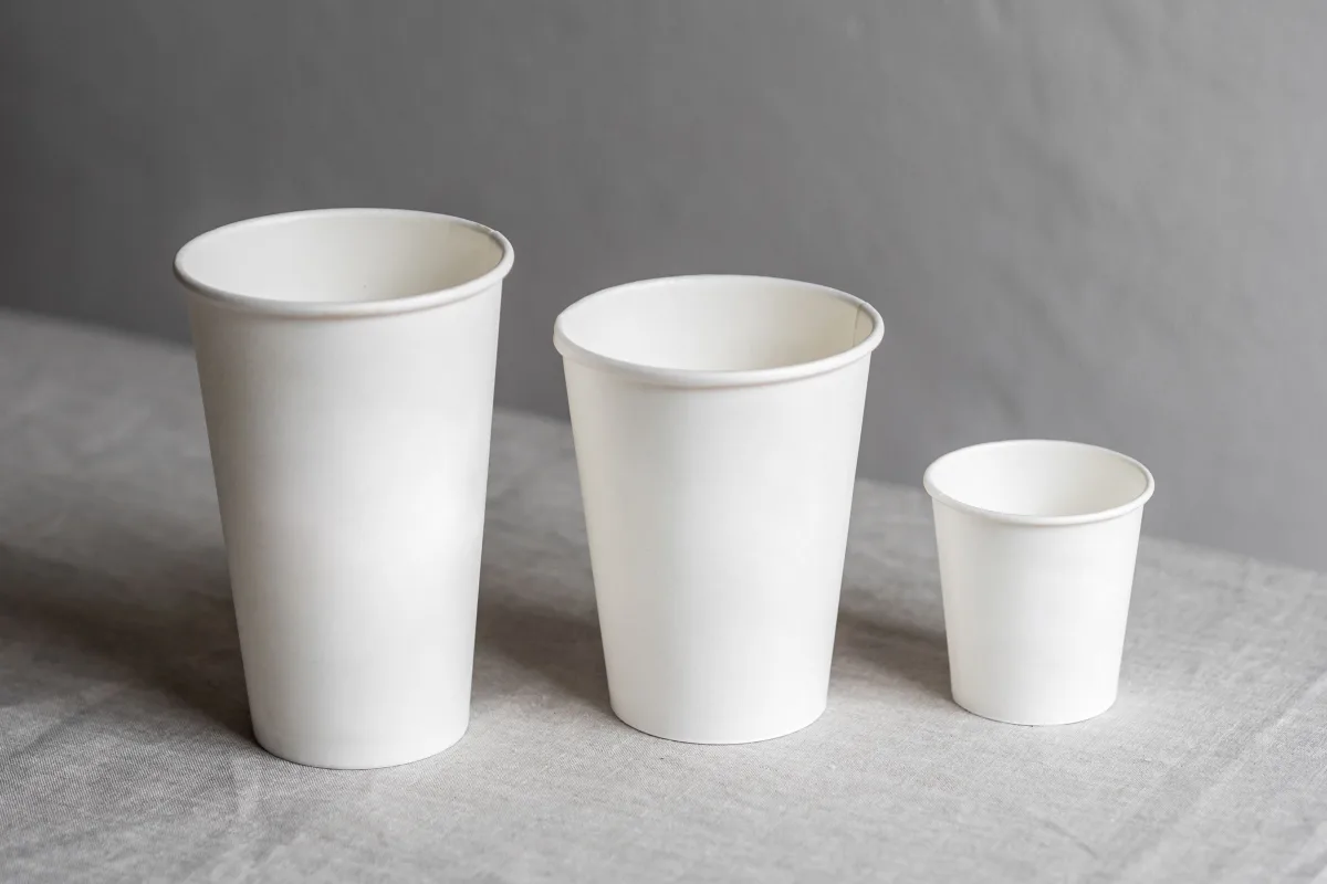 How many ounces in a cup of coffee: three white paper coffee cups, large, medium and small, on a linen table